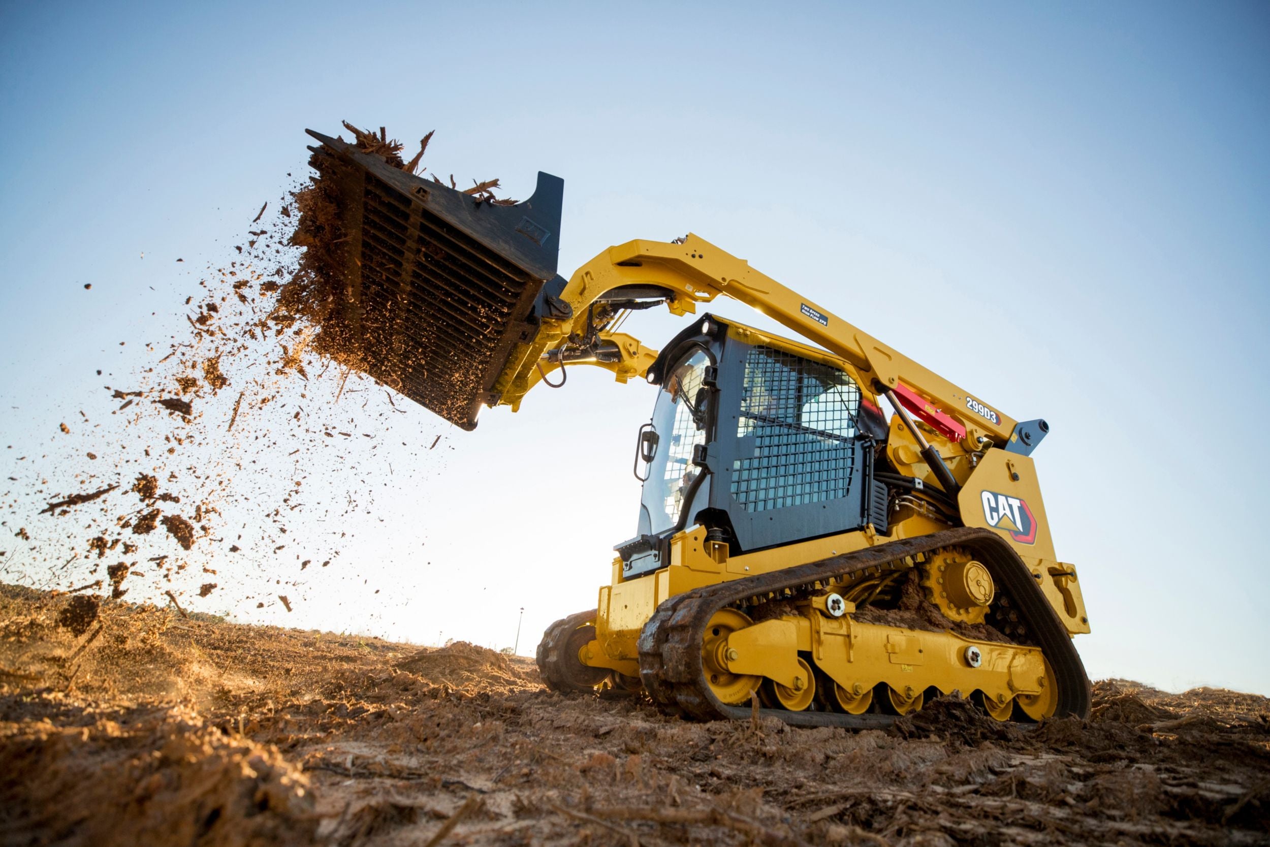 A Cat tracked skid steer lifting dirt against a sunny background.